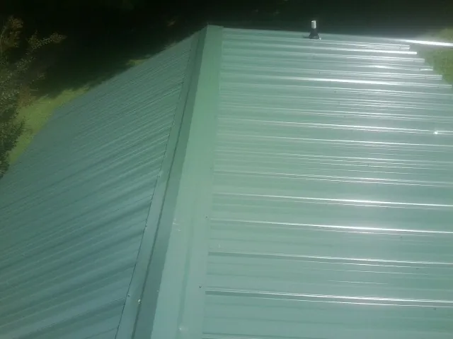 New green metal panels meeting at the ridge of a roof — Flat Roof Repair work by our crew in Jerome