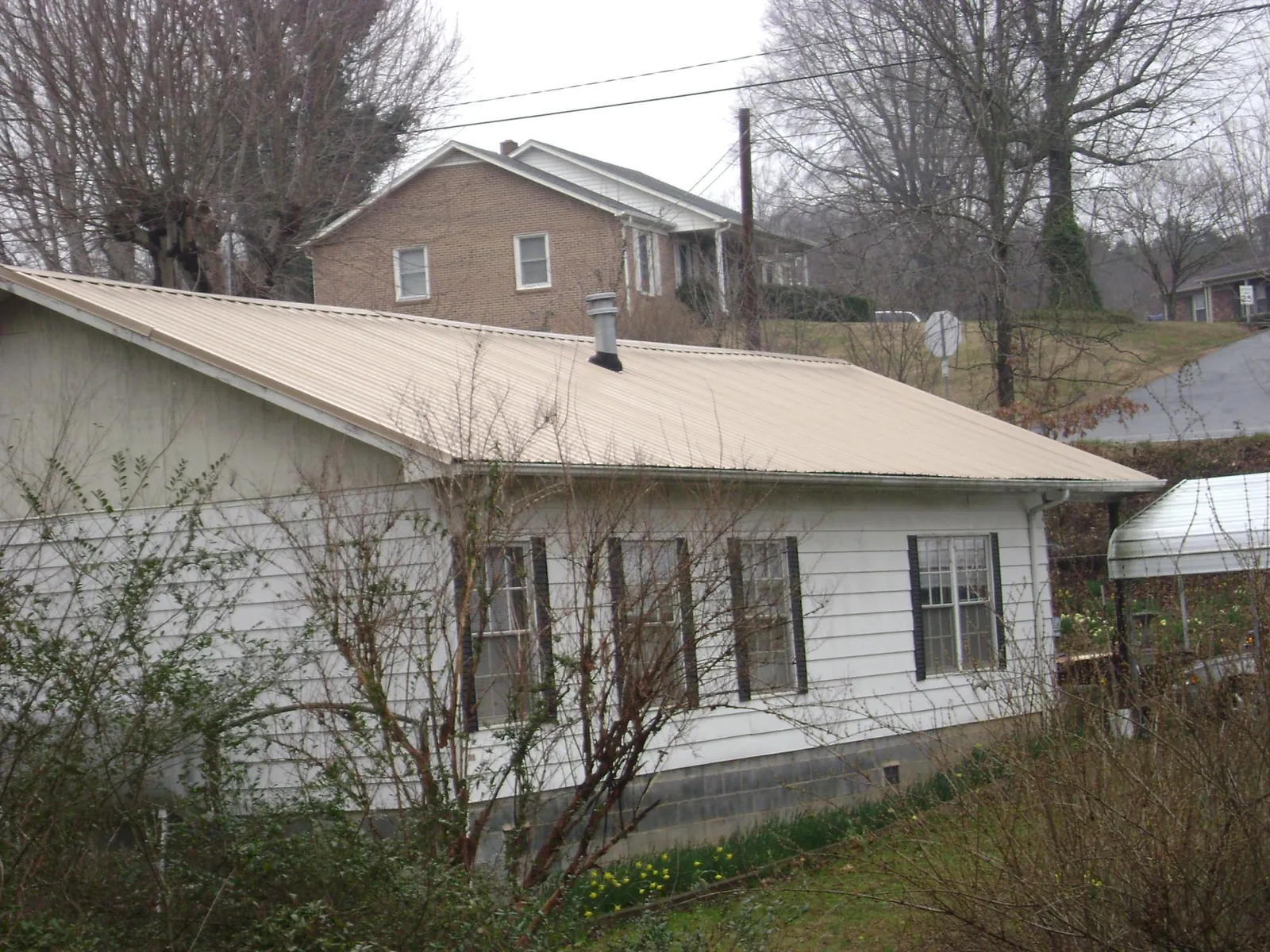 Tan metal roof on a white sided house set into a hillside — Commercial Roofing by Roofing Brothers in Jerome