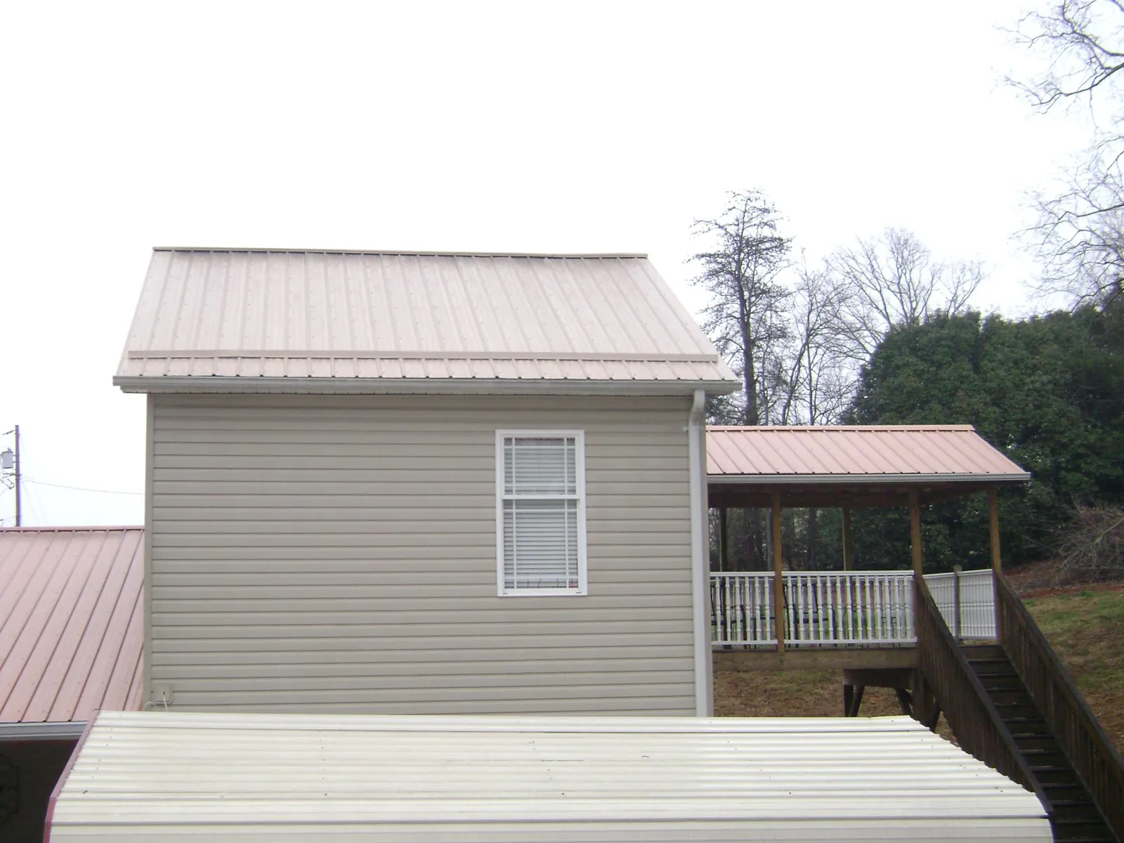 Tan metal roofs on a two story addition and attached porch, from a Roof Replacement job in Jerome